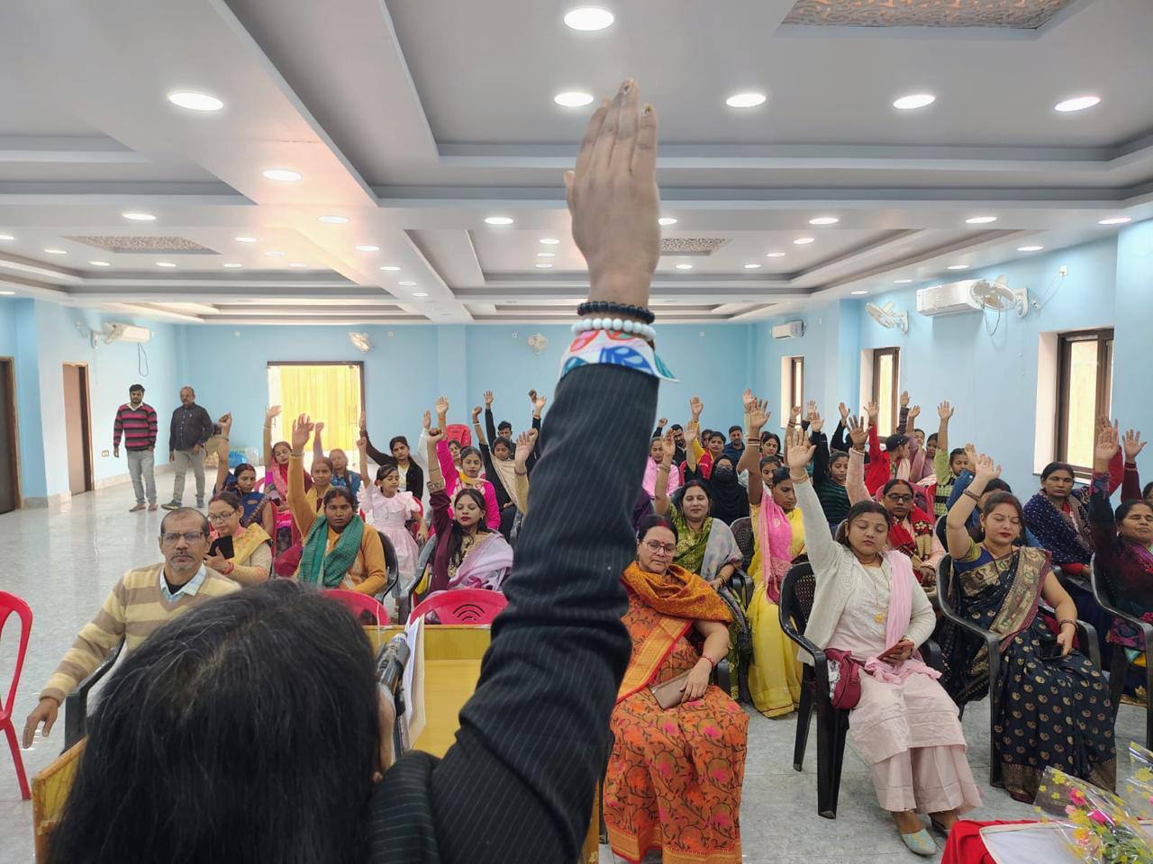 A hall full of participants with hands raised during an exercise
